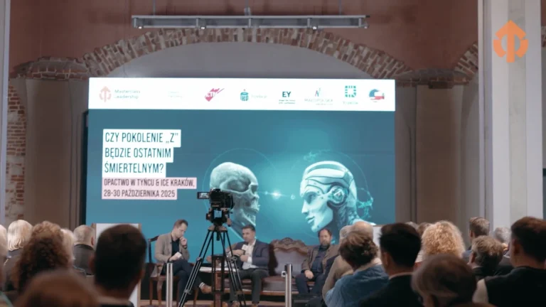 Widownia konferencji, na scenie ekran z prezentacja, przed publicznoscia kamera na statywie