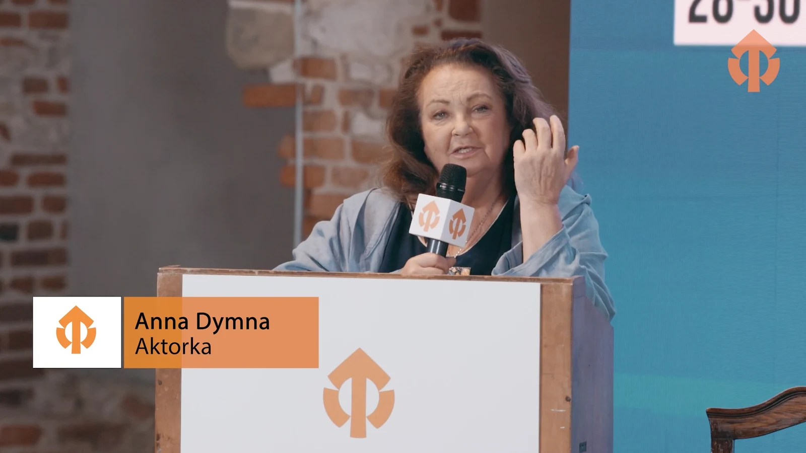 Prelegentka na scenie konferencji, na dole kadru belka z imieniem i funkcją